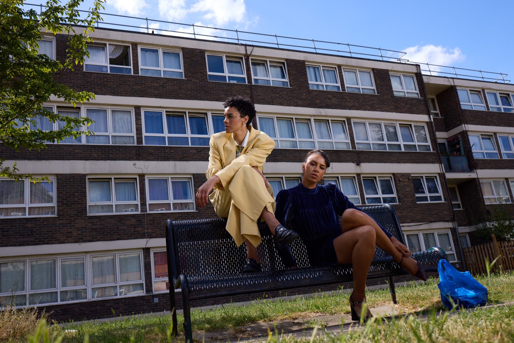 Holly perched on the back of a bench beside Mel, London estate behind them